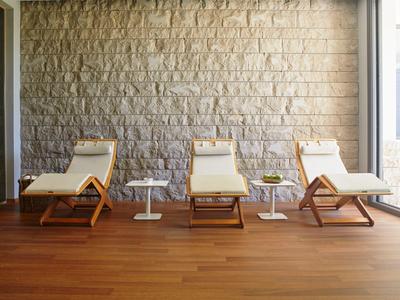 Vier weiße Liegestühle aus Holz stehen vor einer hellen Steinwand auf braunem Holzboden.