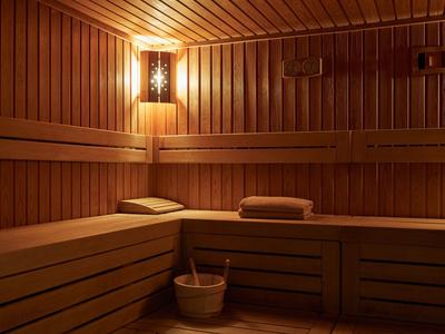Gemütliche Sauna aus hellem Holz mit Holzbänken, Handtüchern, Holzeimer und sanfter Wandbeleuchtung.