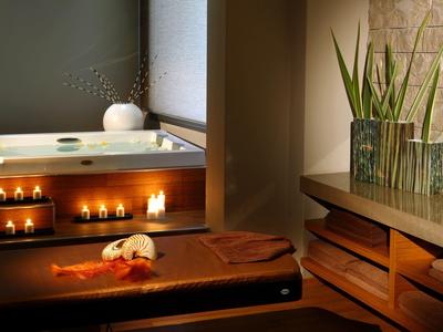 Gemütlicher Wellnessraum mit Holzbank, Kerzen, Pflanzen und warmem Licht.