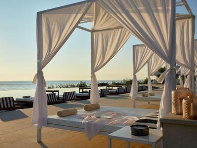 Strand mit luxuriösen weißen Himmelbetten und Blick auf das Meer bei Sonnenuntergang.