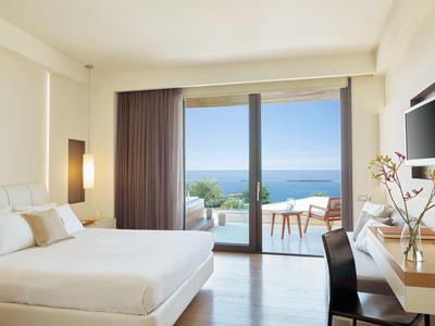 Helles Schlafzimmer mit Doppelbett, großem Balkon und Meerblick bei klarem Himmel.