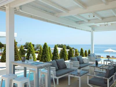 Moderner Terrassenbereich mit weißen Möbeln, Grünpflanzen und Meerblick bei klarem Himmel.