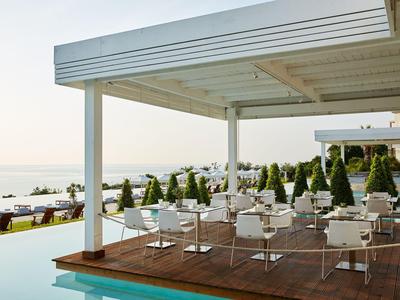 Freiluftrestaurant mit weißen Tischen und Stühlen neben einem Infinity-Pool und Blick auf das Meer.