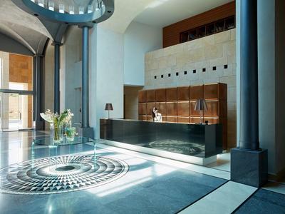 Moderner Empfangsbereich mit Glasfront, Rundteppich, Ledertheke und hellem Steinboden.