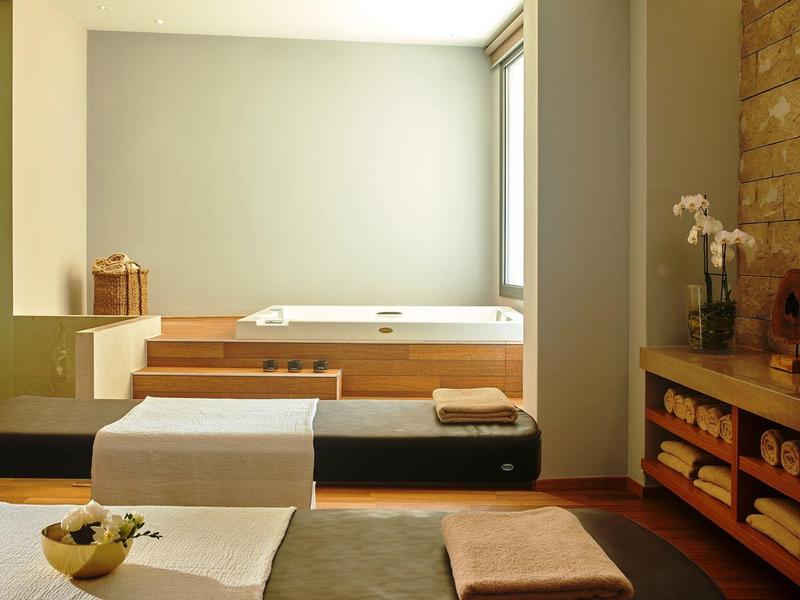 Moderner Wohnraum mit Holzmöbeln, weißen Sitzpolstern, Steinwand und Pflanzen auf Regal.