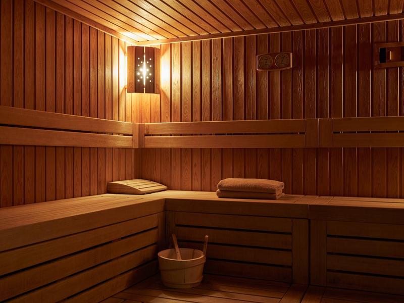 Gemütliche Sauna aus hellem Holz mit Holzbänken, Handtüchern, Holzeimer und sanfter Wandbeleuchtung.