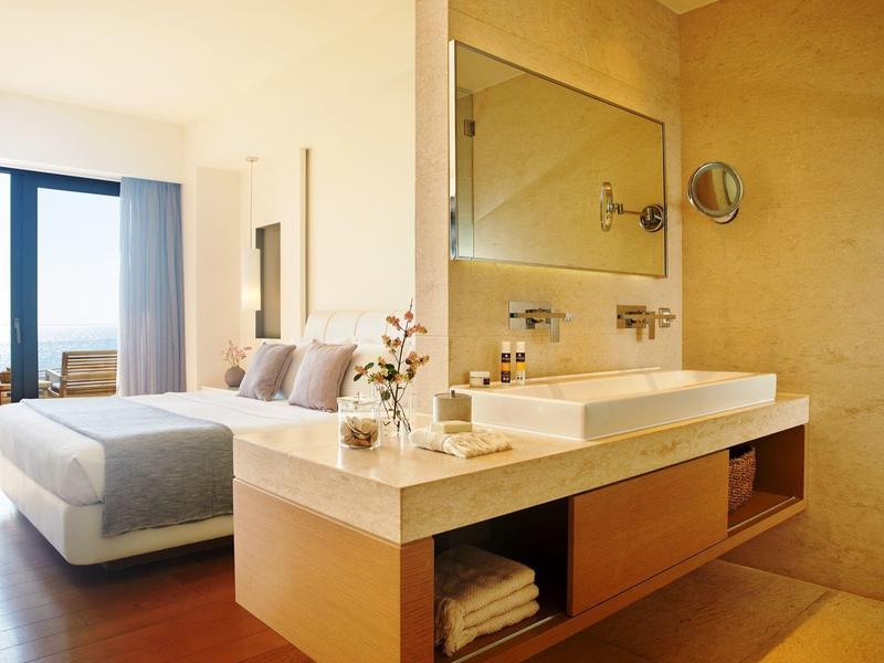 Ein modernes Schlafzimmer mit großem Bett und angrenzendem Bad mit hellem Waschbecken und Spiegel.