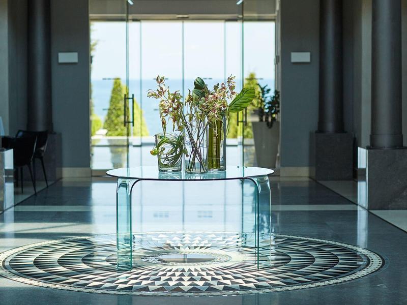 Moderner Eingangsbereich mit großem Glas-Tisch und Pflanzen vor bodentiefen Fenstern und Mosaikboden.