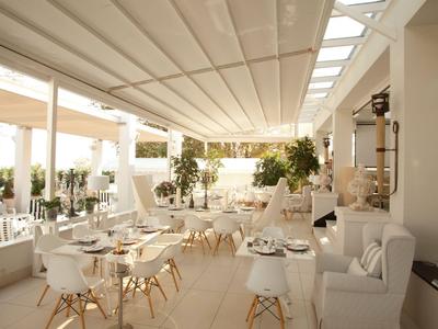 Helle, moderne Terrasse mit weißen Möbeln, Tischen und Pflanzen, ideal für Gäste.