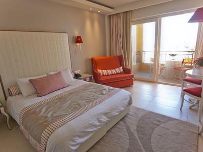 Hell eingerichtetes Hotelzimmer mit Doppelbett, Sofa und Balkon mit Blick nach draußen.