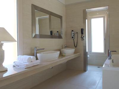 Helles, modernes Badezimmer mit Doppelwaschbecken, großem Spiegel, weißer Badewanne und Fenster.