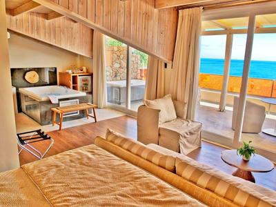 Helles Hotelzimmer mit Holzdecke, gemütlichem Bett, Balkon und Meerblick bei Sonnenlicht.