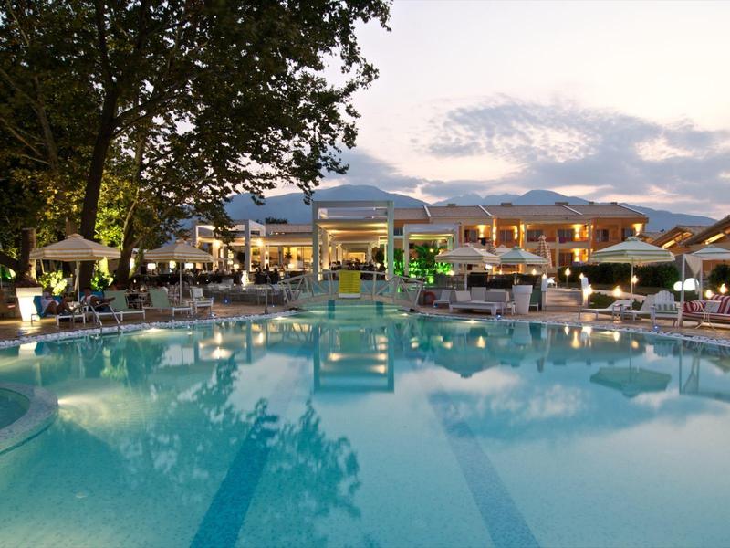 Großer Pool mit klarem Wasser vor beleuchtetem Hotelgebäude in der Abenddämmerung.