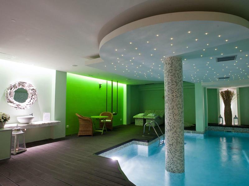 Moderner Innenpool mit rundem Säulendach, grünen Wänden und bequemen Sitzbereichen.