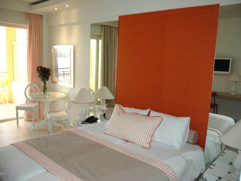 Modernes Schlafzimmer mit großem orangenem Kopfteil, weißem Bett und kleinem Tisch mit Stühlen.