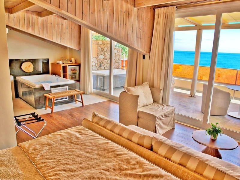 Helles Hotelzimmer mit Holzdecke, gemütlichem Bett, Balkon und Meerblick bei Sonnenlicht.