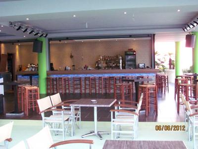 Heller Barbereich mit Holzhockern und weißen Stühlen in einem Hotel oder Restaurant.