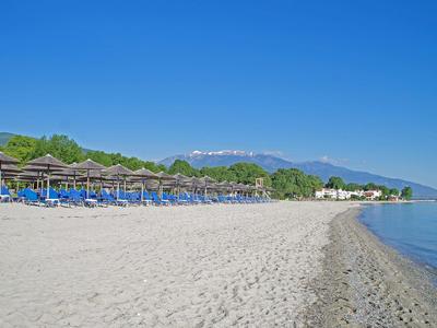 Ein ruhiger Sandstrand mit blauen Sonnenschirmen, klarer Himmel und Bergen im Hintergrund.