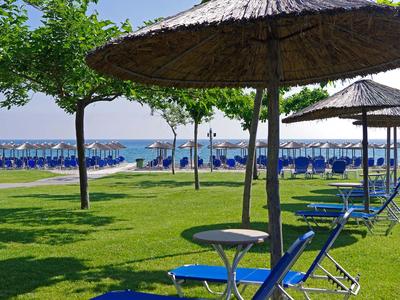 Grüne Liegewiese mit Sonnenschirmen und blauen Liegestühlen am Strand.