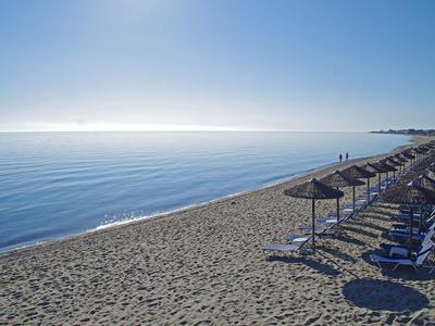 Leerer Sandstrand mit Sonnenschirmen und Liegestühlen unter blauem Himmel am ruhigen Meer.