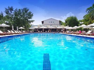 Großer Hotelpool mit Sonnenliegen und Sonnenschirmen an einem sonnigen Tag.