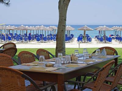 Blick auf einen gedeckten Holztisch im Freien mit Meer und Strandstühlen im Hintergrund