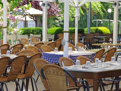 Freiluftrestaurant mit geflochtenen Stühlen und blau-weiß karierten Tischdecken unter Sonnenschirmen.