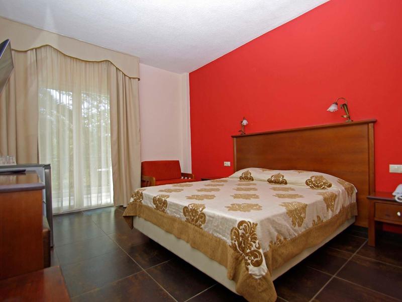 Ein Hotelzimmer mit einem Doppelbett, roten Akzenten und einem Fenster mit Vorhängen.