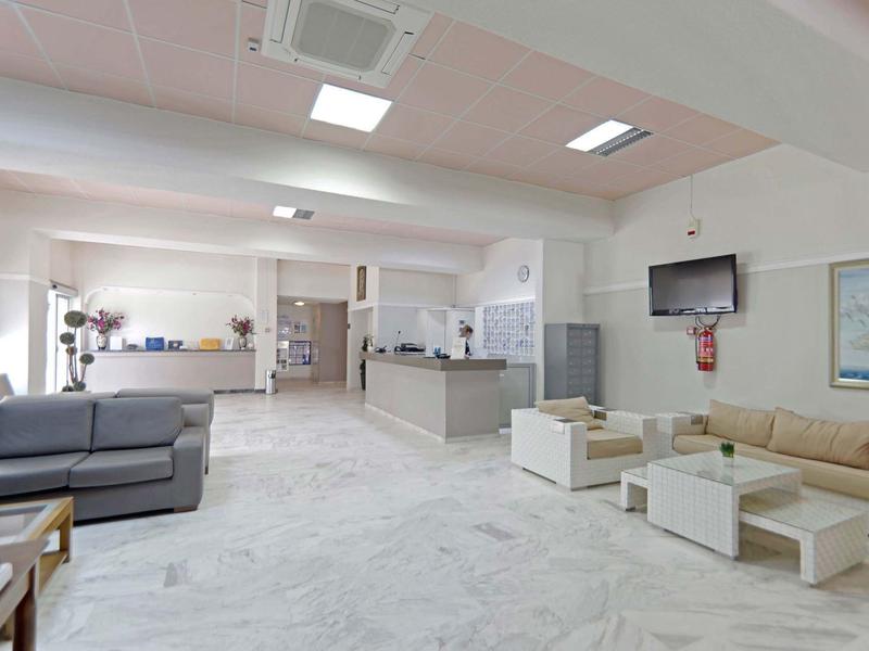 Heller, moderner Empfangsbereich mit Sitzgelegenheiten, Rezeption und Fernseher an der Wand.