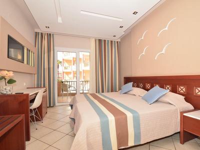 Helles Schlafzimmer mit Doppelbett, bunten Vorhängen, Schreibtisch und Balkon mit Geländer.