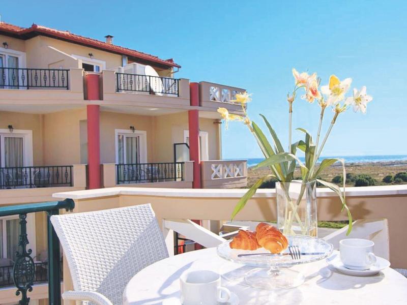 Balkontisch mit Blumen, Frühstücksgedeck und Mehrfamilienhaus im sonnigen Hintergrund.