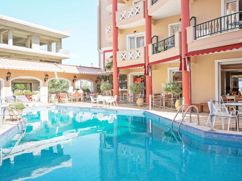 Heller Innenhof mit rechteckigem Pool, weißen Stühlen, Tischen und einem mehrstöckigen Gebäude.