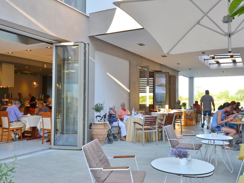 Moderner Außenbereich eines Cafés mit Sitzgruppen, Tischen und Gästen unter überdachtem Bereich.