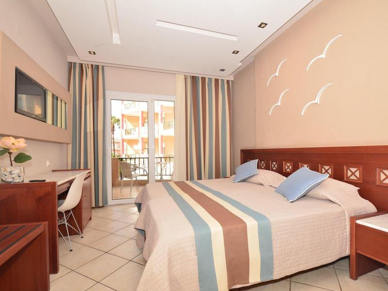 Helles Schlafzimmer mit Doppelbett, bunten Vorhängen, Schreibtisch und Balkon mit Geländer.