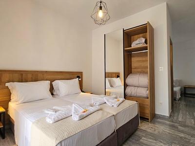 Helles Schlafzimmer mit Doppelbett, Holzkopfteil, offenem Schrank und grauem Fliesenboden.