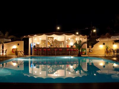 Beleuchtete Bar mit Sitzplätzen neben großem, ruhigem Pool in der Nacht.