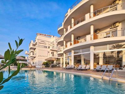 Hôtel moderne avec piscine, chaises longues et ciel dégagé du matin.