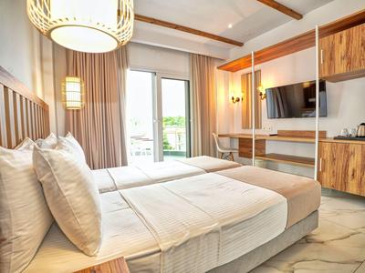 Modernes Hotelzimmer mit Doppelbett, Fernseher, Schreibtisch und kleinem Balkon.