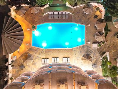 Beleuchteter Pool mit Liegestühlen, Sonnenschirmen und spiralförmiger Treppe, umgeben von Natur.