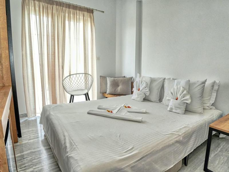 Hell eingerichtetes Schlafzimmer mit großem Bett, weißen Kissen und Holz-Möbeln neben Vorhangfenster.