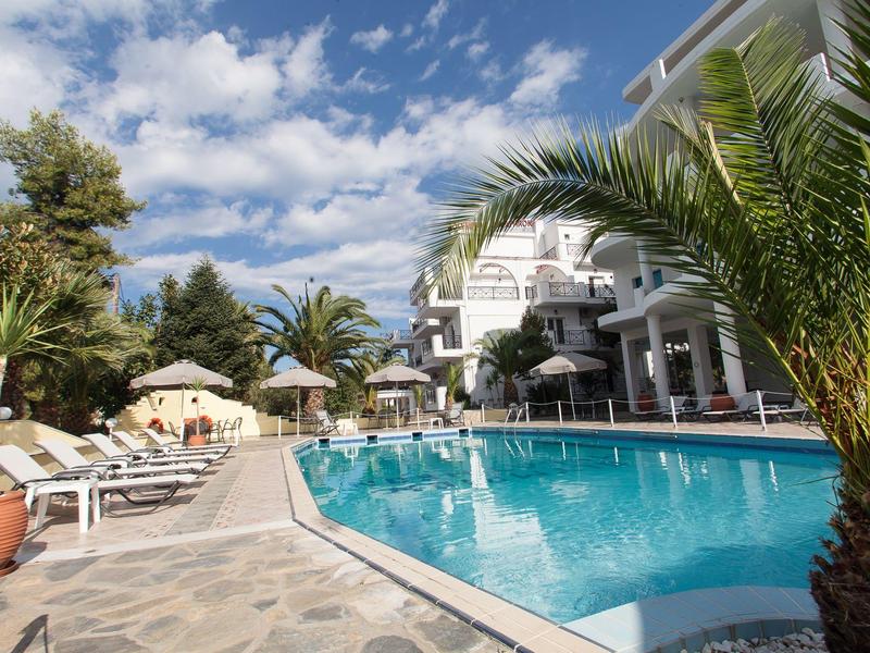 Ein klarer Pool umgeben von Palmen, Liegestühlen und einem weißen Gebäude im Hintergrund.