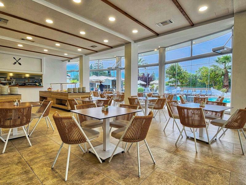 Moderner Innenraum mit Holztischen, Stühlen und großen Fenstern, die Pool und Garten zeigen.