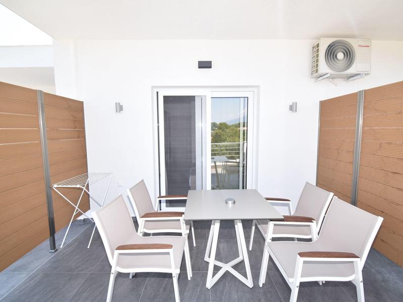 Moderner Balkon mit grauem Boden, sechs weißen Stühlen mit rosa Sitzkissen und grauem Tisch.