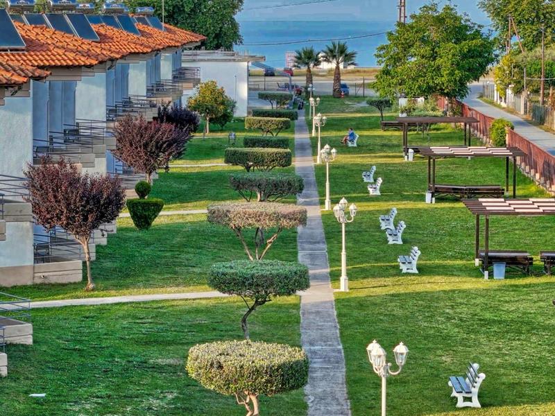 Reihenhäuser mit grünen Gärten, Bänken und schattigen Bäumen entlang eines Gehwegs.