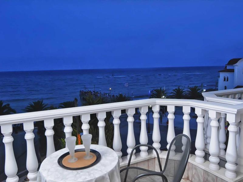 Balkon mit weißem Geländer, runder Tisch, Stühlen und Blick auf das blaue Meer bei Dämmerung.