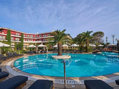 Piscina redonda de hotel rodeada de tumbonas, palmeras y un edificio de tres pisos bajo un cielo azul.