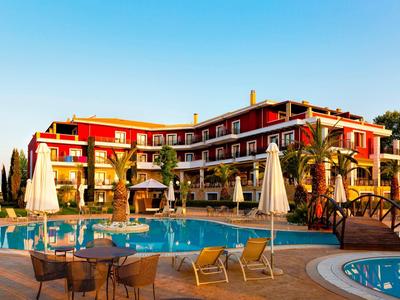 Hotelgebäude mit roten Wänden, Pool, Liegestühlen und Sonnenschirmen unter blauem Himmel.