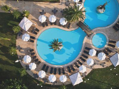 Vista aérea de un hotel exótico con piscina curva y sombrillas blancas.