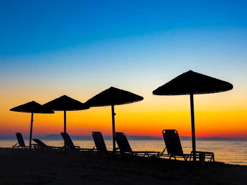 Strand mit Liegestühlen und Sonnenschirmen, Sonnenuntergang mit blau-orangem Himmel am Meer.