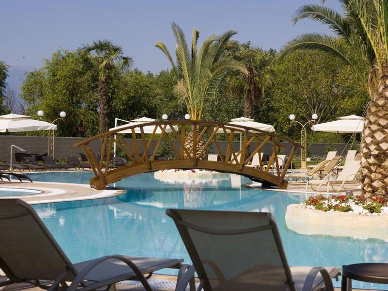 Schwimmbad mit blauem Wasser, Liegestühlen, weißen Sonnenschirmen und kleinem Holzbrückchen.